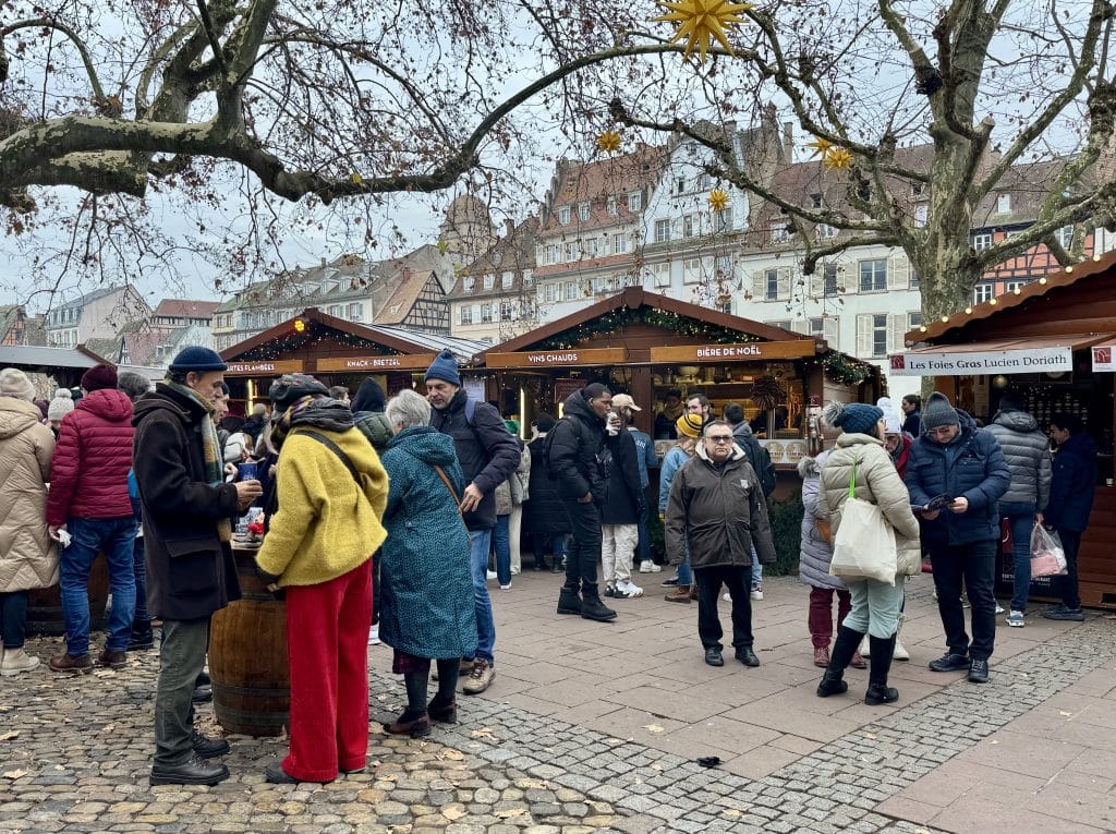 A group of people standing and eating around several wooden chalets serving Alsatian food.