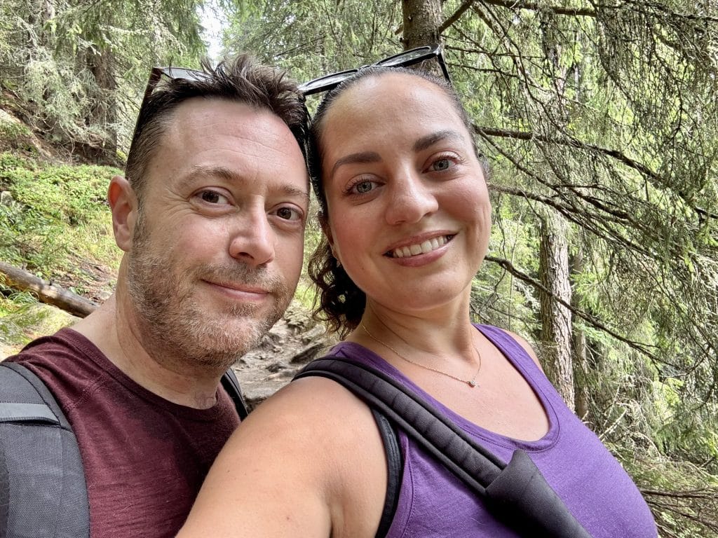 Kate and Charlie taking a smiling selfie while hiking through the woods.