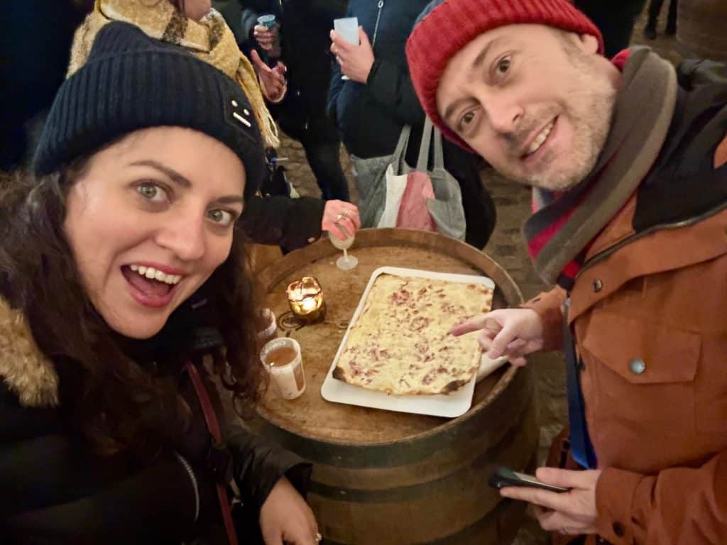Kate and Charlie taking a selfie with big grins with an Alsatian tarte flambé in front of them.