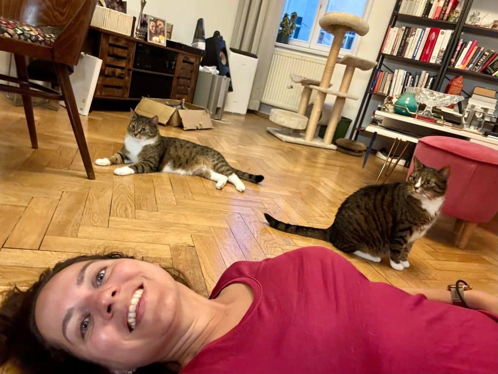 Kate lying on the floor while her gray tabby cats, Lewis and Murray, lie on the floor behind her.