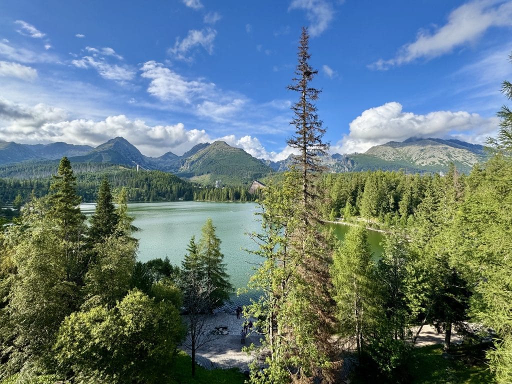 The view from above a still turquoise lake edged with mountains and pine trees.