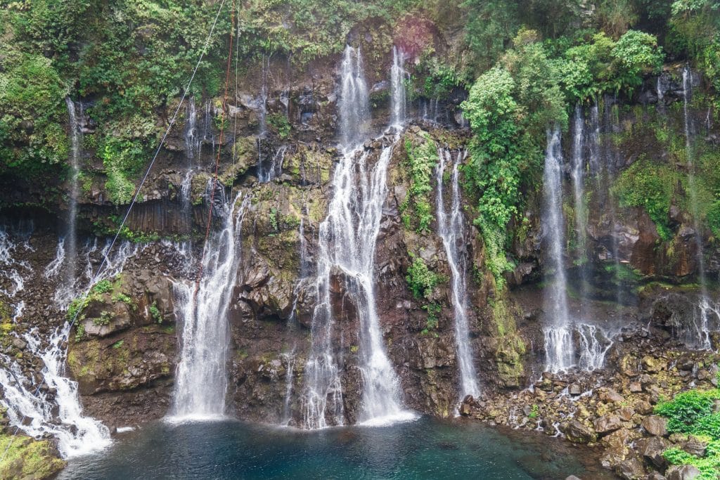 A large waterfall with several thin veils falling into a clear teal pool.