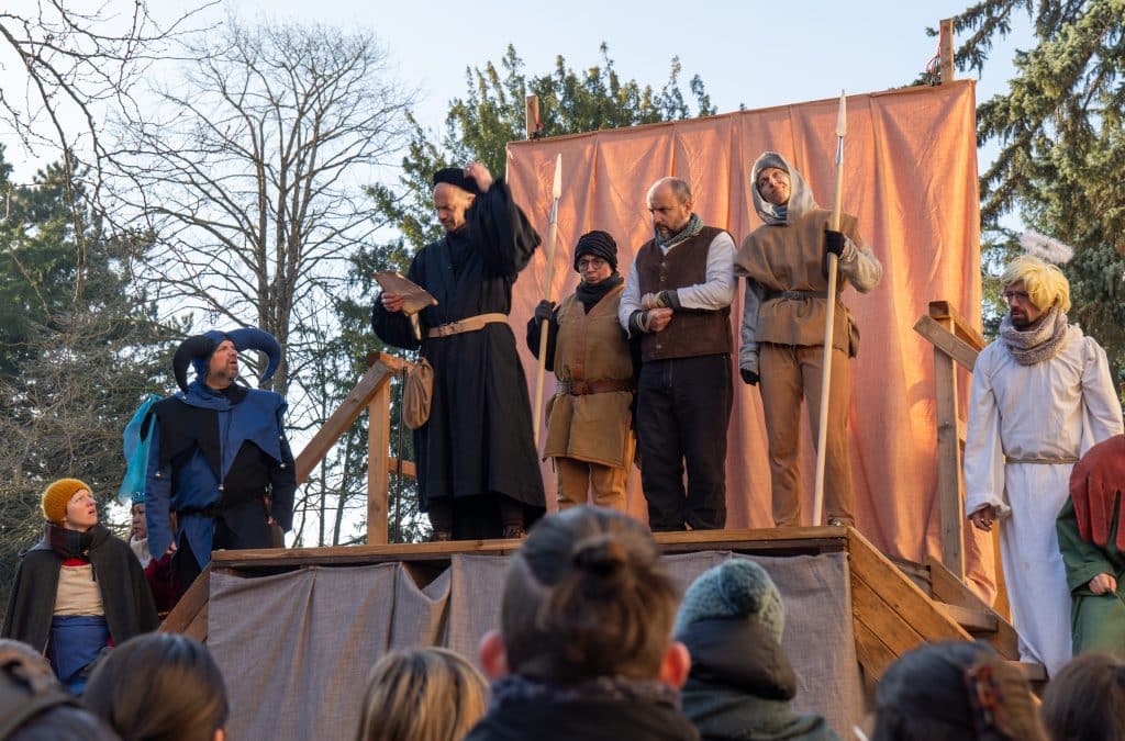 A group of people dressed as monks and jesters on stage, acting out for an audience.