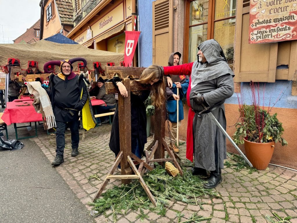 A medieval knight locking a woman in the stocks, her head and hands pointing through the holes.