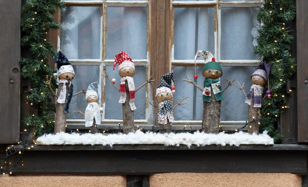 A window topped with snowman-like decorations carved from wood.
