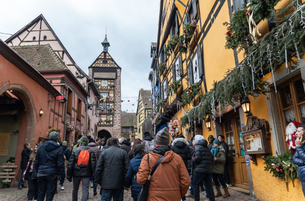 Crowds of people walking down the street with a yellow building covered with Christmas lights and garlands.