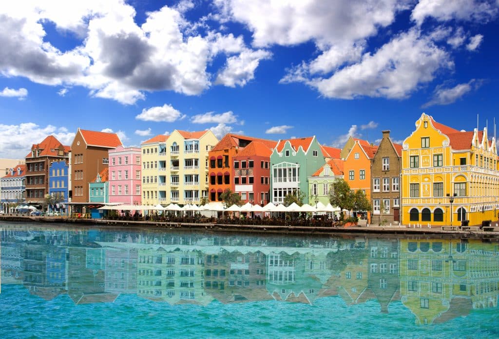 A row of bright, colorful Dutch-style houses perched on the turquoise water of Curacao's harbor.