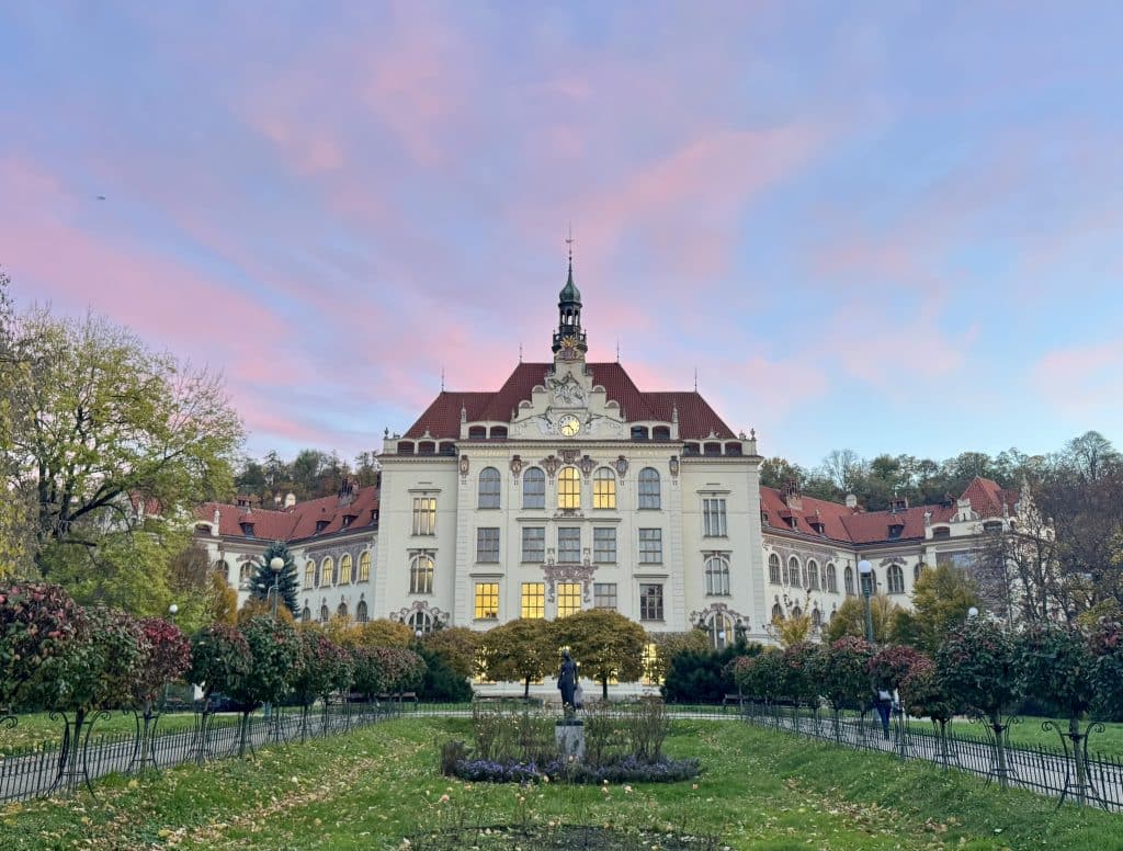 An old-fashioned white and brown building in Prague in front of a pink and blue sunset.