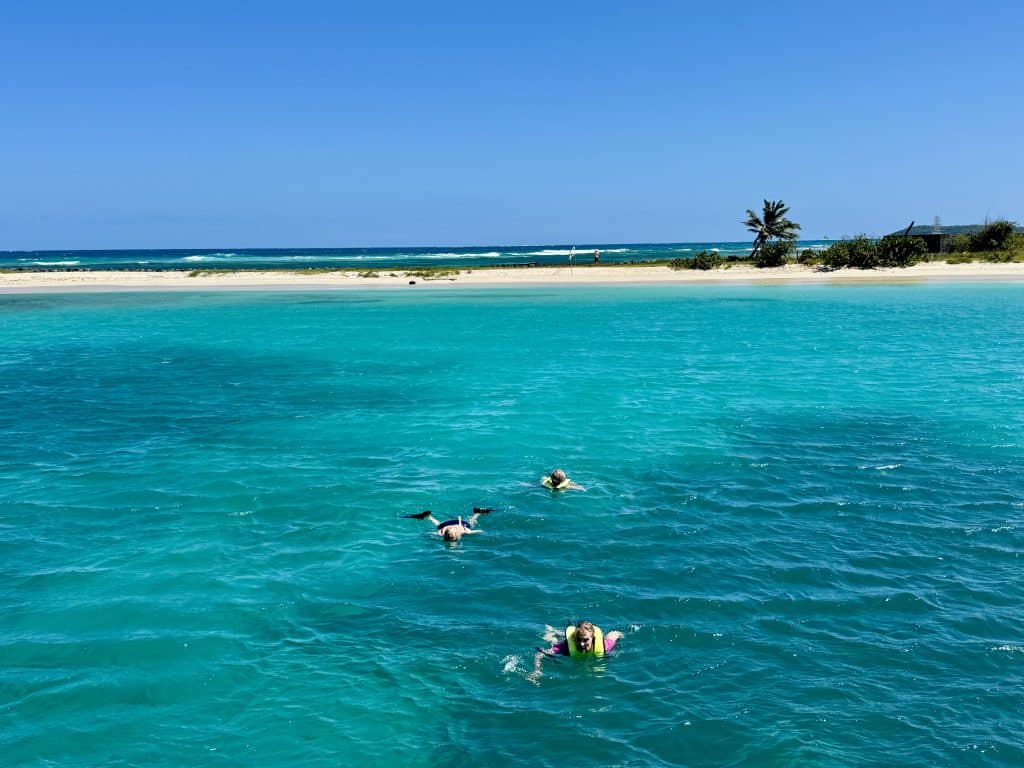 Three people swimming away from a beach in calm, bright turquoise water.