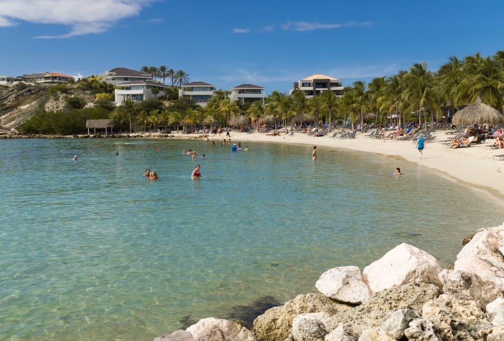 A crescent-shaped beach with extremely calm water in a very pale aquamarine shade.