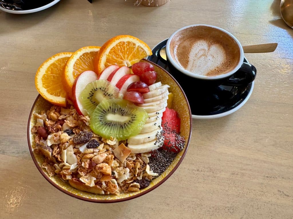 A granola and fruit-topped bowl and cappuccino at a cafe.