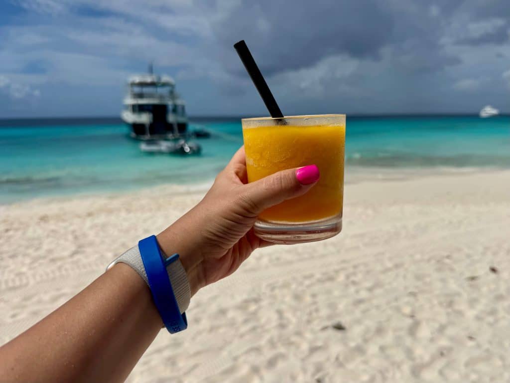 Holding up a mango cocktail on a beach.