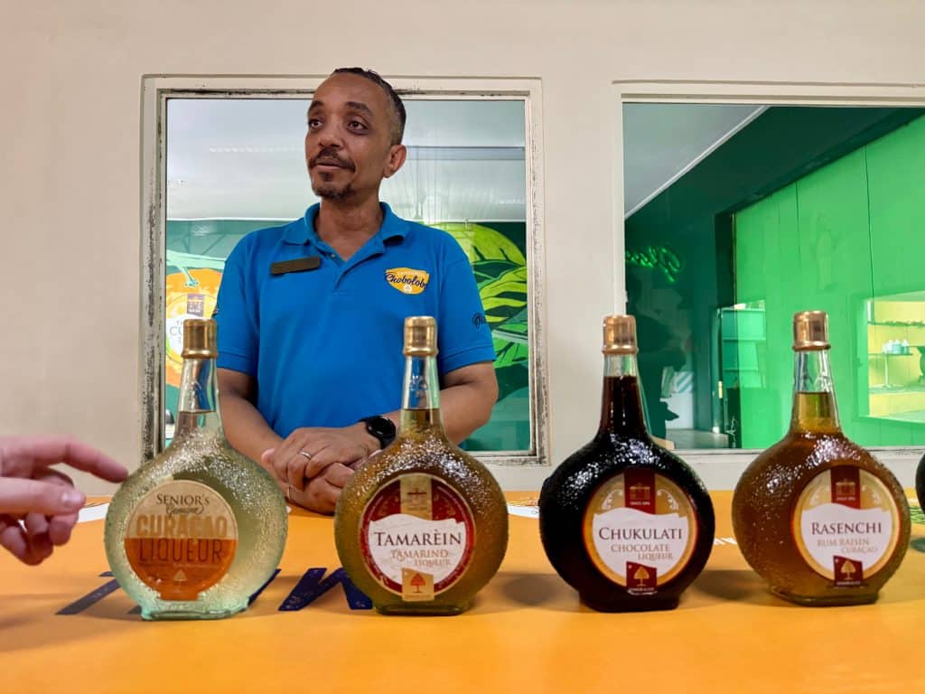 A guide standing behind several round bottles of Curacao liqueur in various shades of brown.