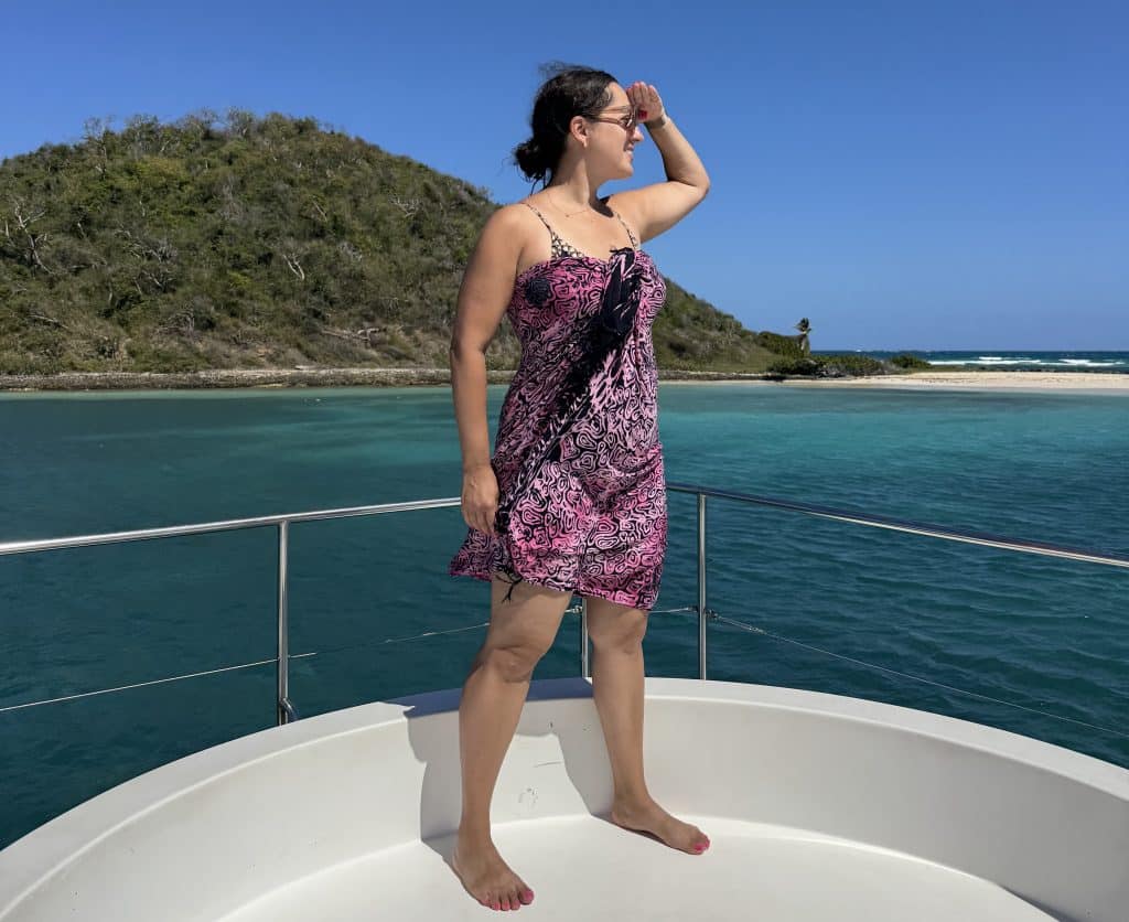 Kate standing on a boat in a pink and black sarong, holding her hand above her eyes as if looking ahead.