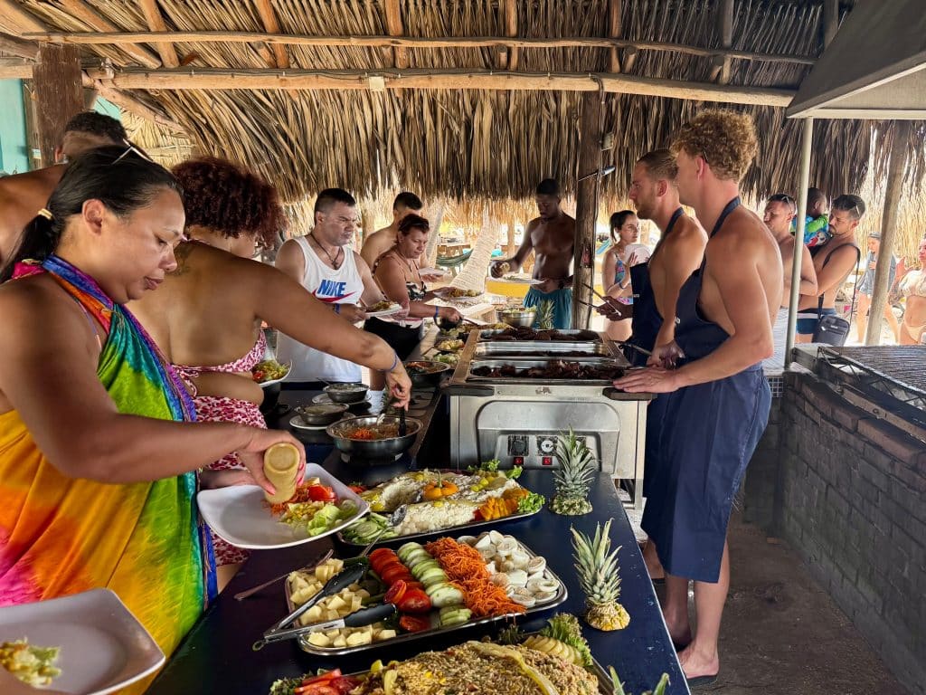 Two shirtless Dutch dudes in aprons serving barbecue to a crowd.