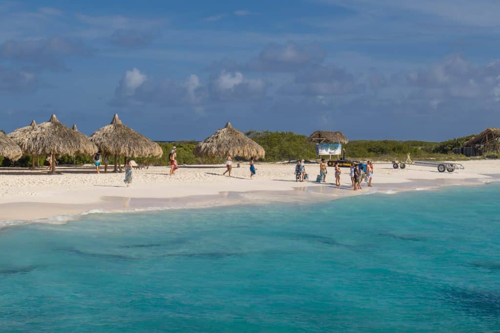 A small island with white sand beaches, clear blue water, and a few huts on shore.