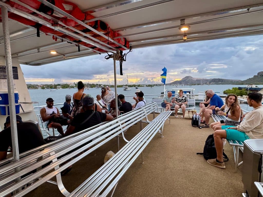 A top deck on a boat with long white benches and people of all ages hanging out.