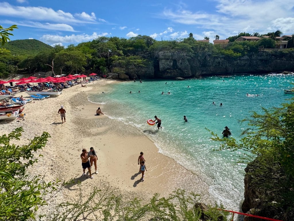 People waling down a calm beach leading to bright turquoise water with gentle waves.