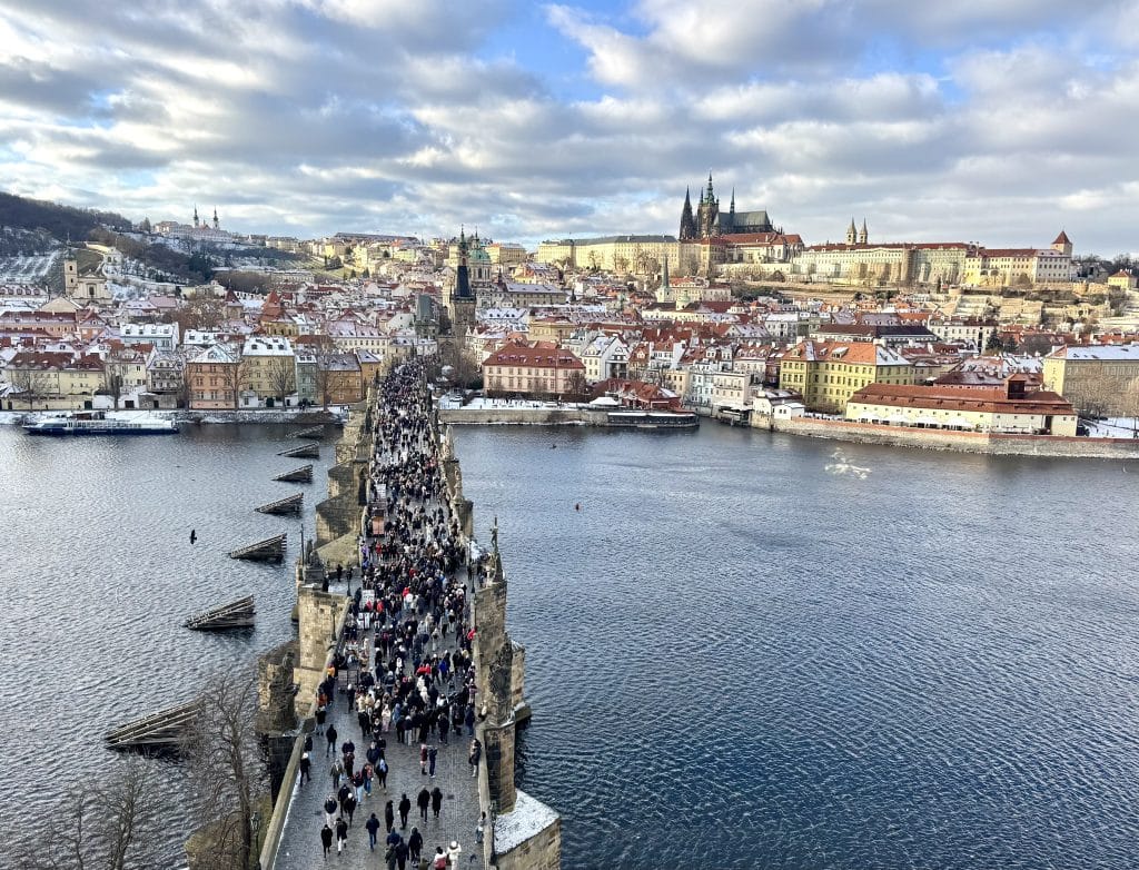 A view of Prague Castle and the Charles Bridge. The rooftops are dusted with snow.