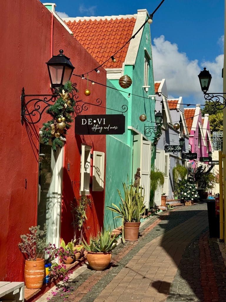 A narrow alley in Curacao lined with homes in. bright red, turquoise, dark purple, and hot pink.