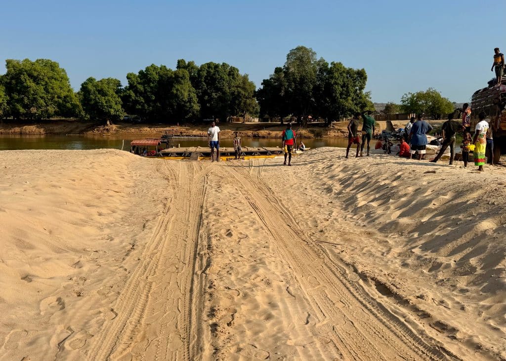 A big, sandy track with tire marks in it leading to a river.
