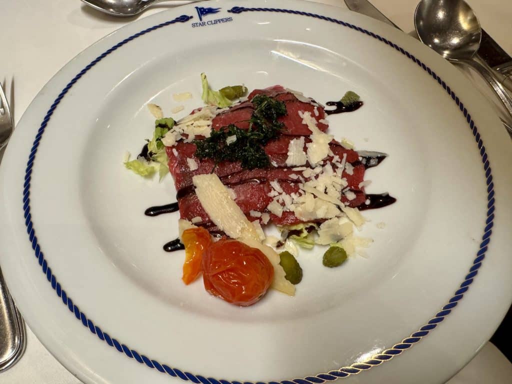 A plate of beef carpaccio topped with parmesan and balsamic vinegar.