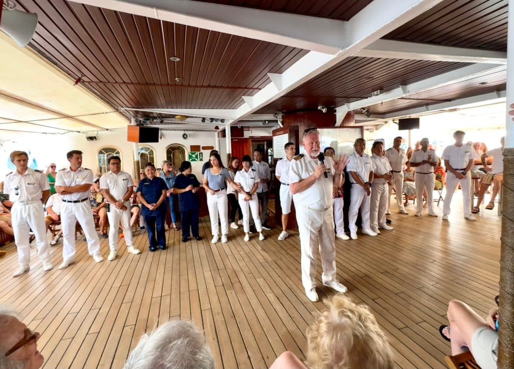Captain Sergey, in his sixties with white hair, standing in front of the crew and giving a talk to the ship.