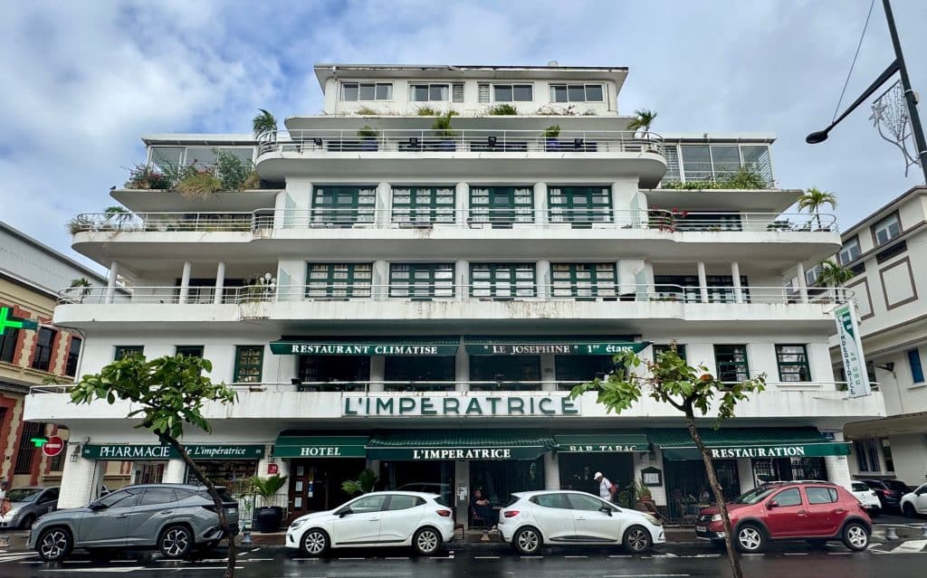 A modern art deco building in Martinique with lots of horizontal windows, five floors, lots of covered balconies and lots of outdoor houseplants.