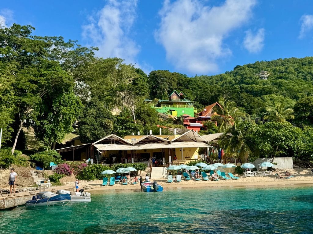A bar set on a beach next to a pier, with several green and white-striped umbrellas out front.