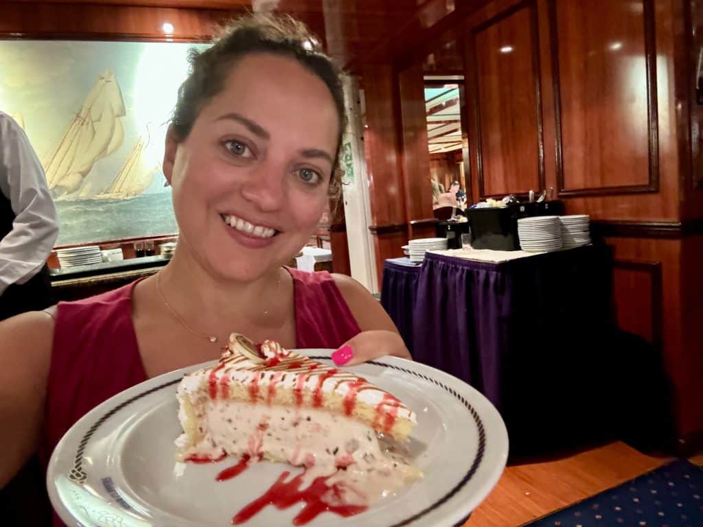 Kate holding a baked Alaska with layers of meringue, yellow cake and vanilla ice cream topped with strawberry syrup.