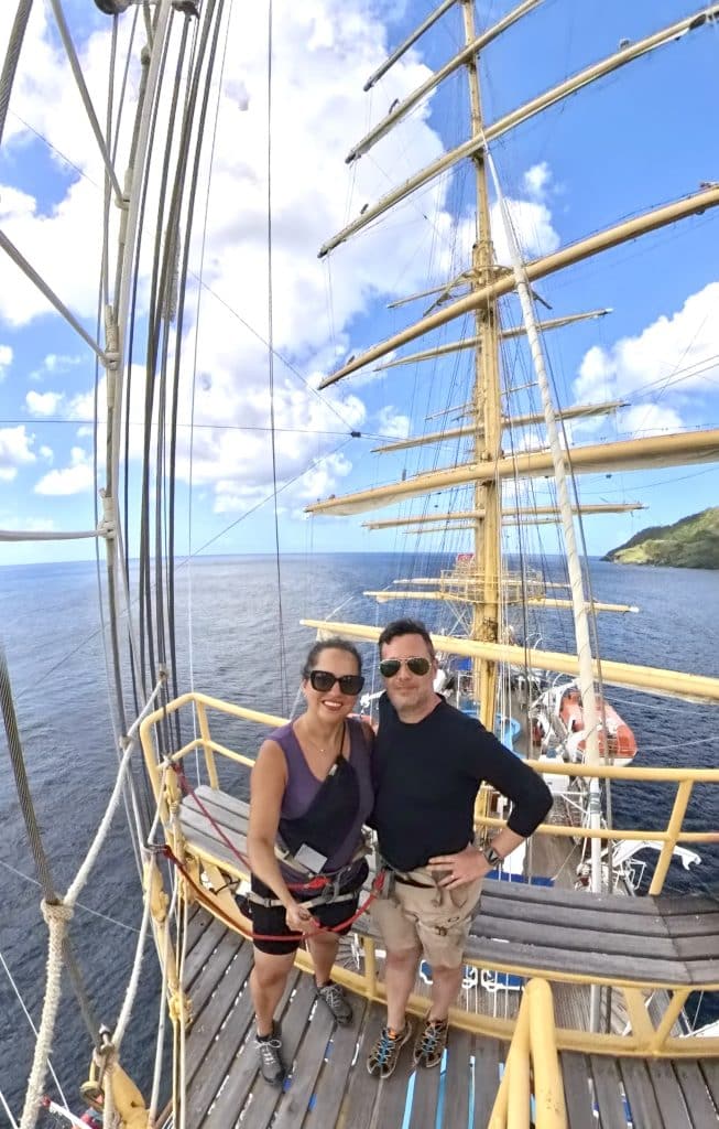 Kate and Charlie smiling side by side in the crow's nest. You can see a few masts behind them, and the ocean below.