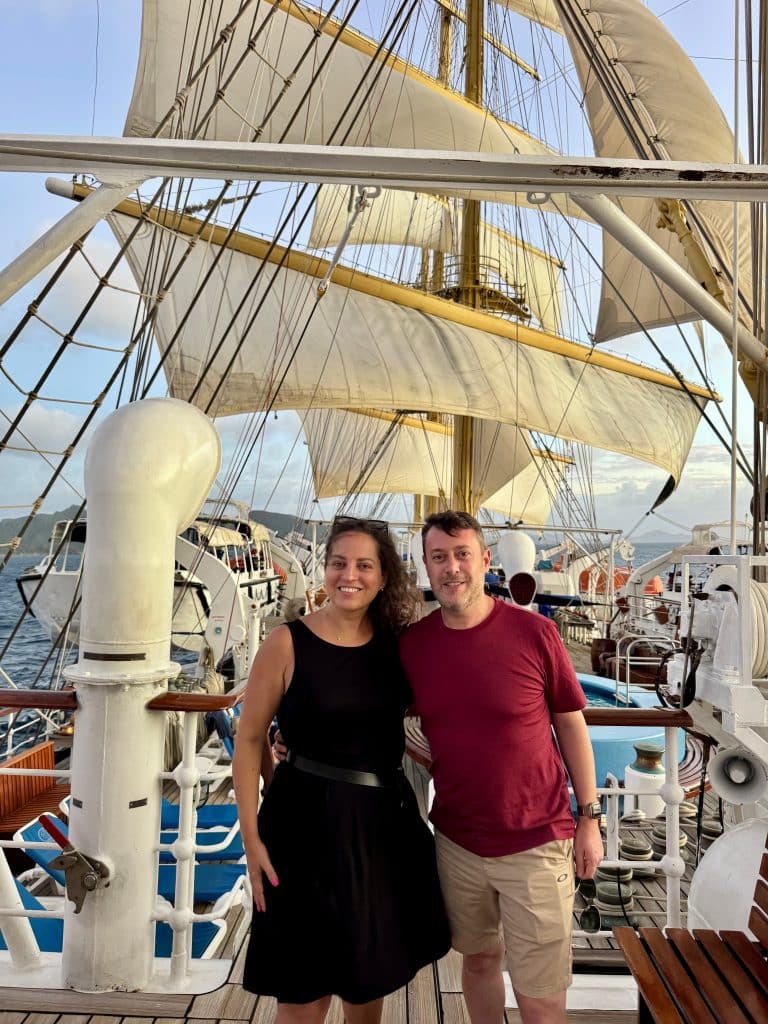 Kate and Charlie standing arm in arm in front of the sails on the Royal Clipper.