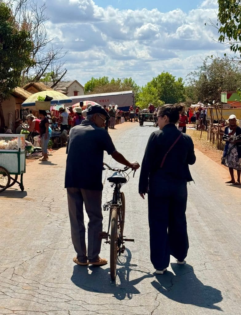 Kate walking down a village street next to an older man walking his bicycle.