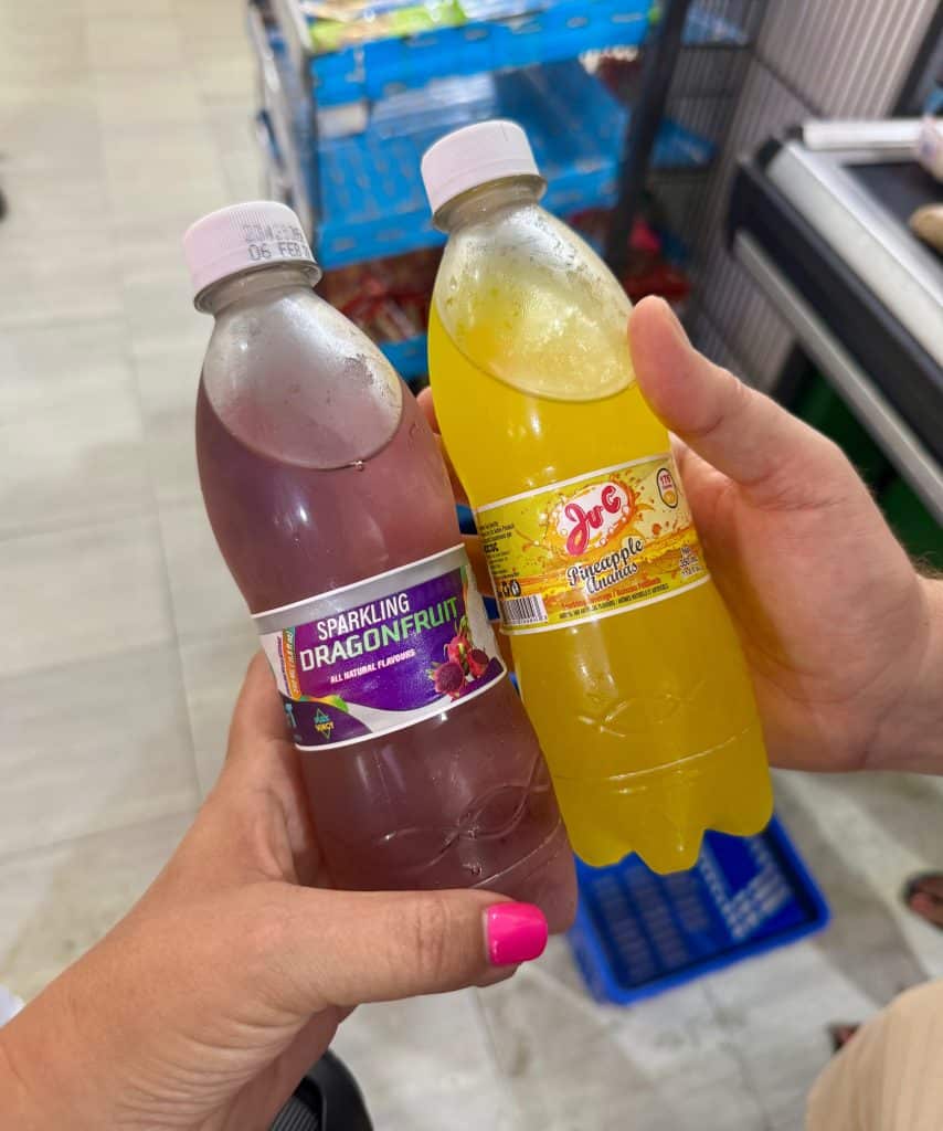 Two hands holding sodas: a purple dragonfruit soda and a yellow pineapple soda.