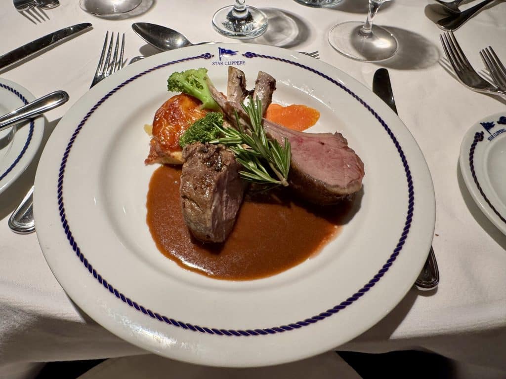 Two pieces of lamb sitting in a brown gravy with a sprig of rosemary and some vegetables.