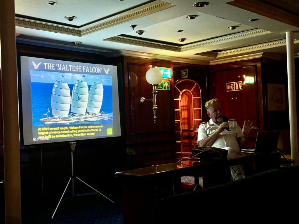 Captain Sergey sitting at a table with a three-masted sailboat on a screen behind him.