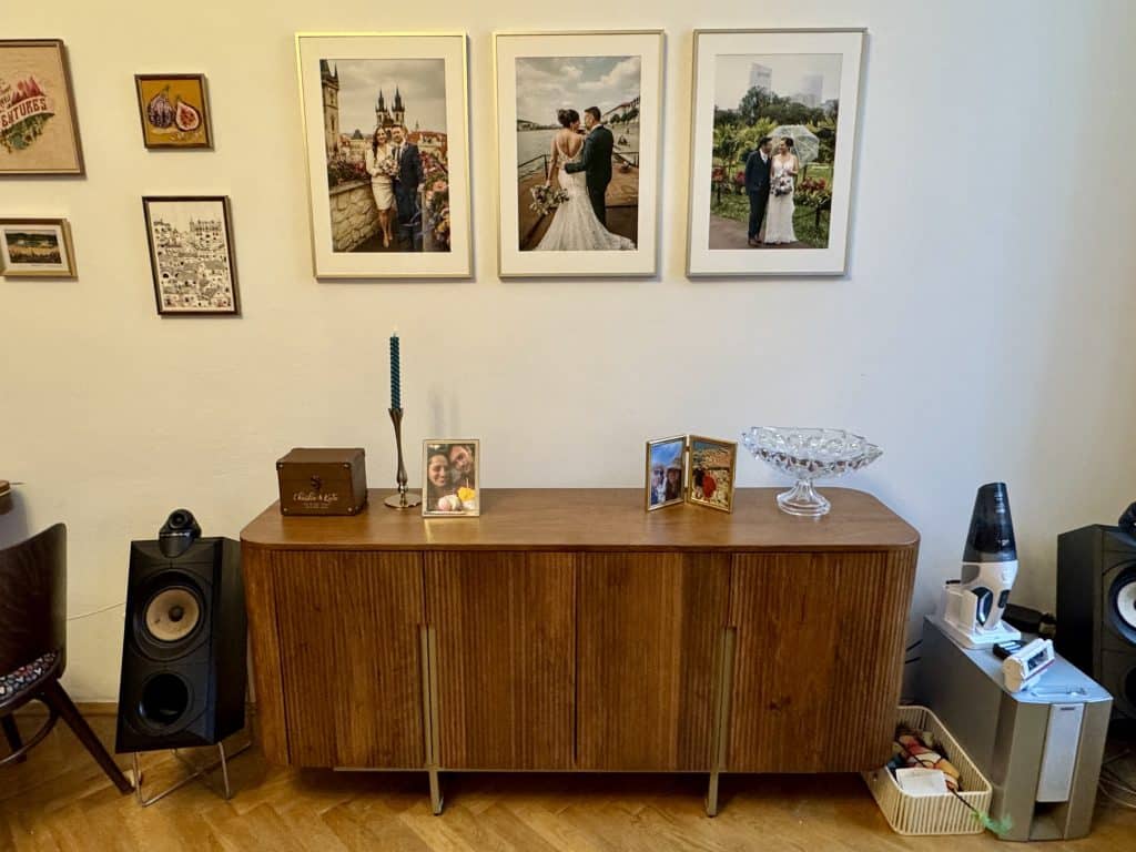 A tall mid-century modern console table in a warm shade of mahogany, with thin gold legs. Three wedding photos above it.