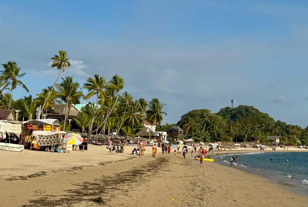 A beach in Madagascar with lots of palm trees and people walking down the beach.