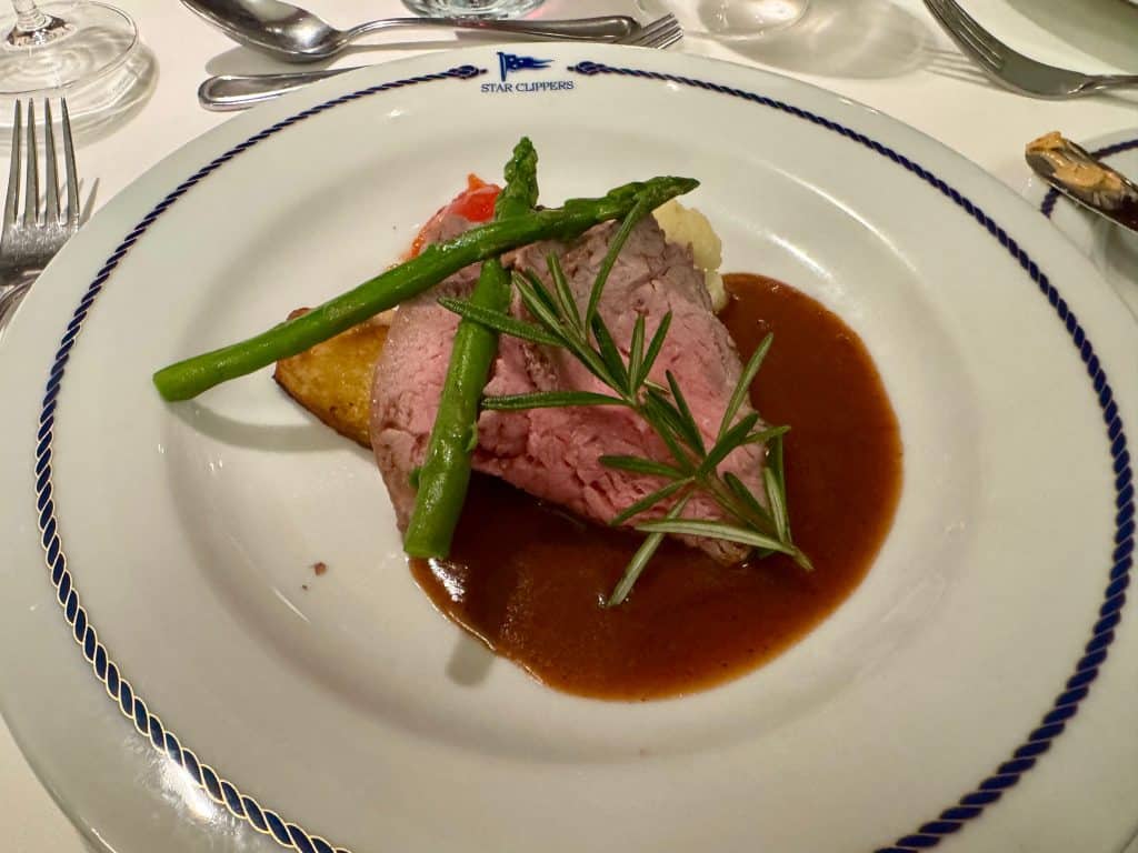 A piece of roast beef sitting gravy, topped with a sprig of rosemary and some asparagus.