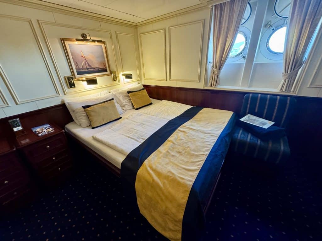 A small cabin with a queen-sized bed against the wall, next to two small porthole windows.