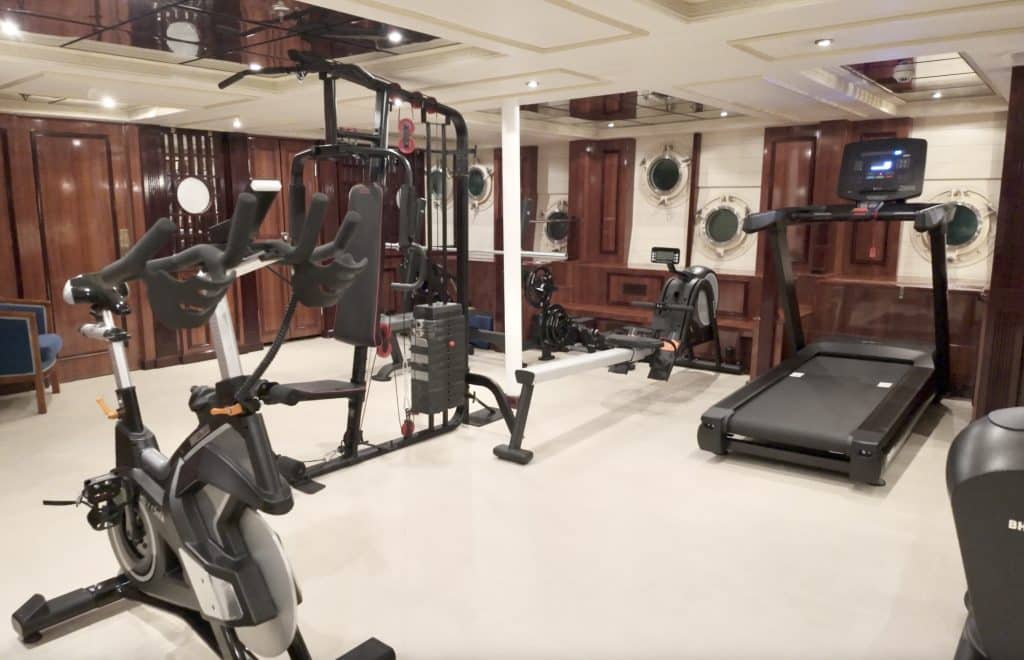 A small gym in a room with portholes and several pieces of cardio equipment.