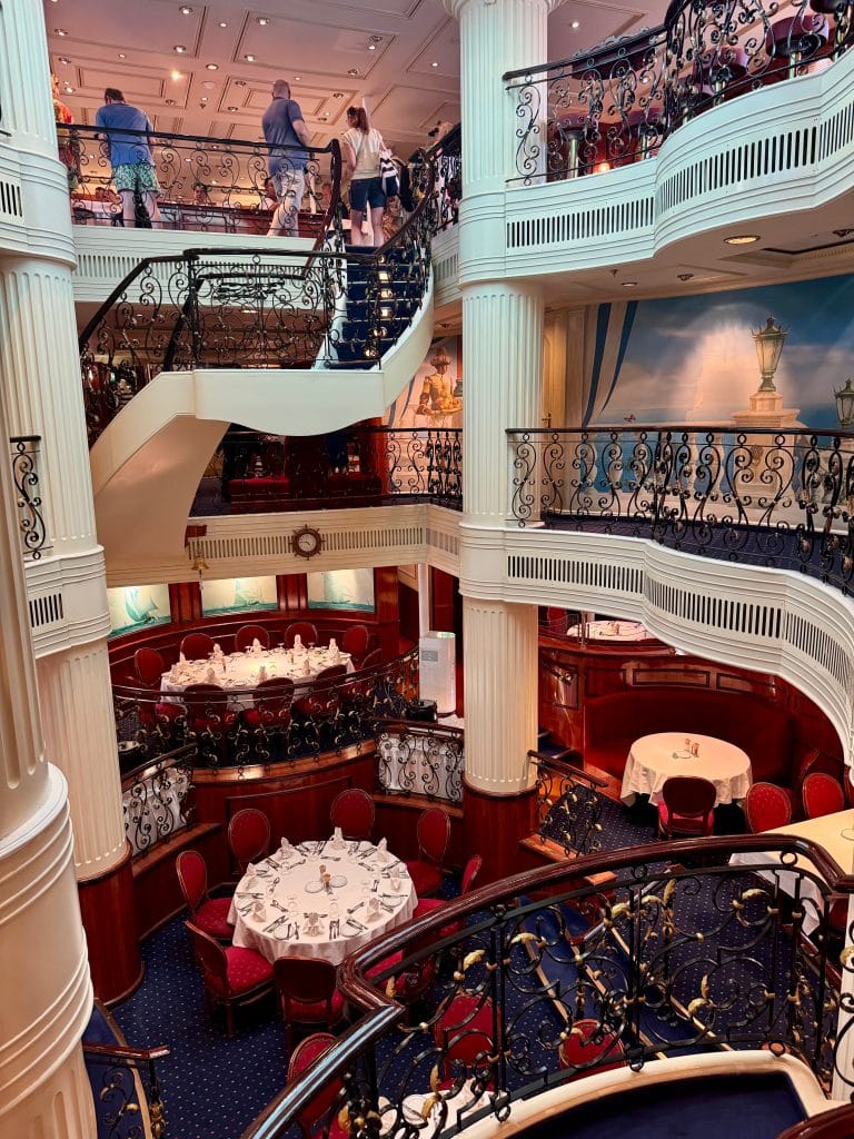 An elegant, multi-floor dining room outfitted in scarlet and white, big tables, and wrought-iron railings.