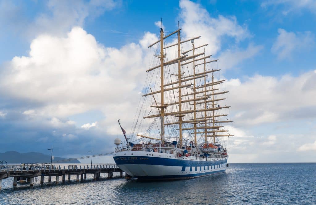 The tall Royal Clipper docked on a pier off the coast of Martinique on a partly cloudy day.