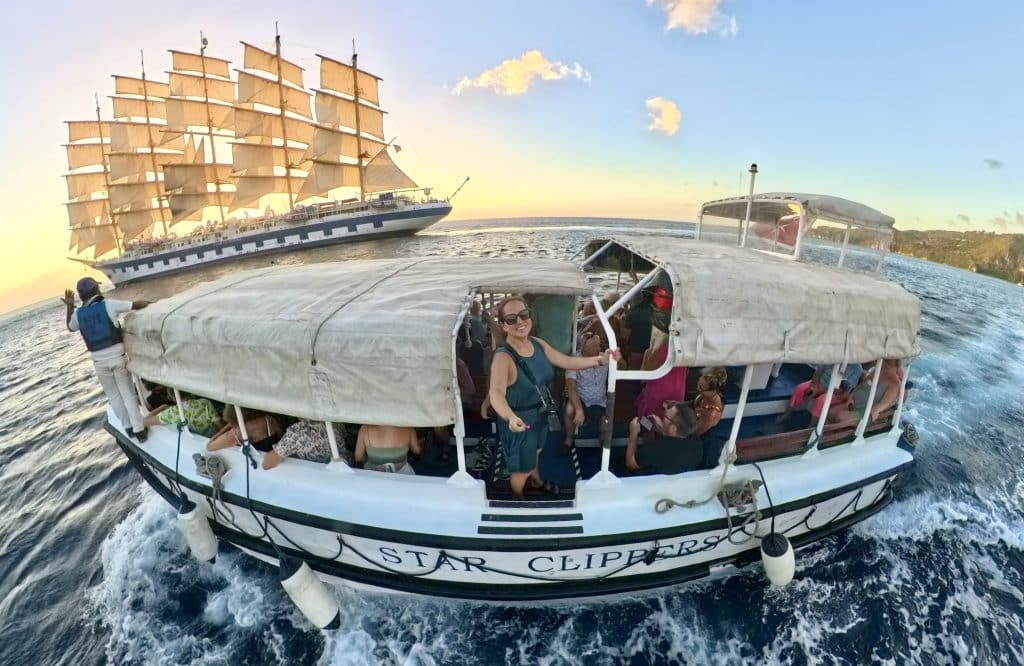 Kate leaning out the door opening of a small tender boat, with the Royal Clipper in t he background, illuminated by the sunset, its sails in full glory.