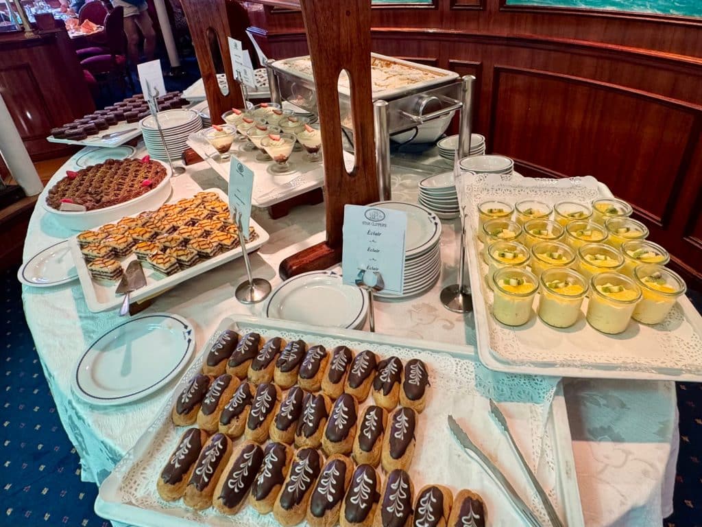 A buffet with mini eclairs, tiny pots of yellow mousse, and little brown cakes.