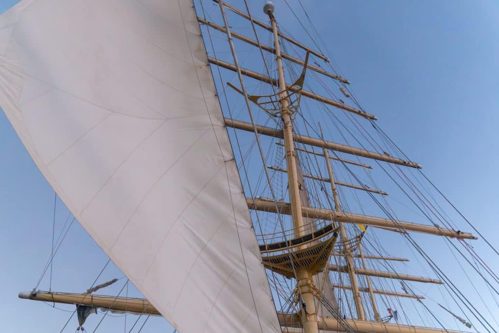 The mast of the Royal Clipper at dawn, with a moody blue sky, and one white sail billowing.