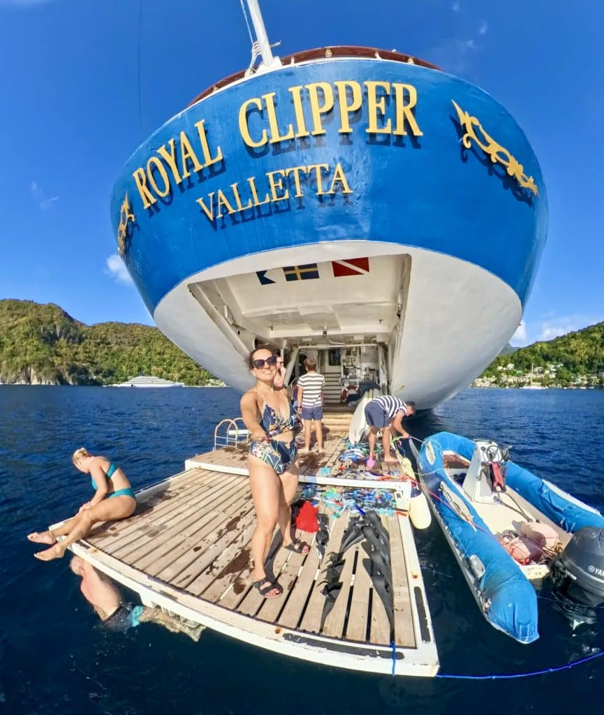 Kate in a bathing suit standing on a platform on the water, the ship behind her, the words "Royal Clipper Valletta" in gold on a bright blue background.