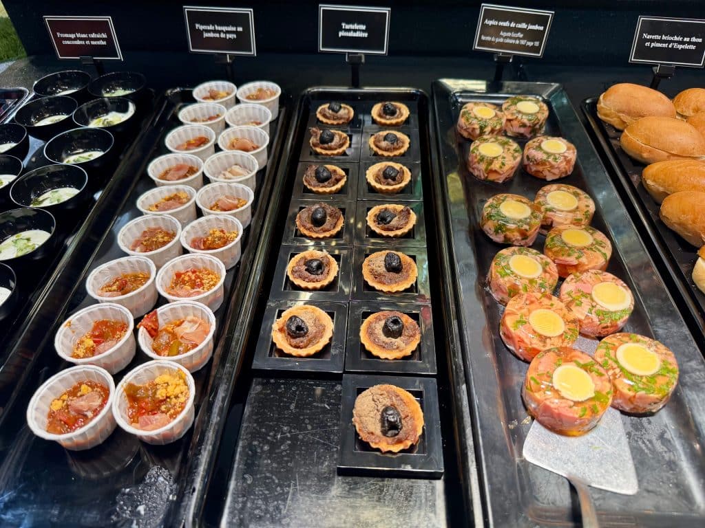 Several small appetizers on a plate, including Basque piperade soup, a little tartlet, and round aspics with ham and eggs inside them.