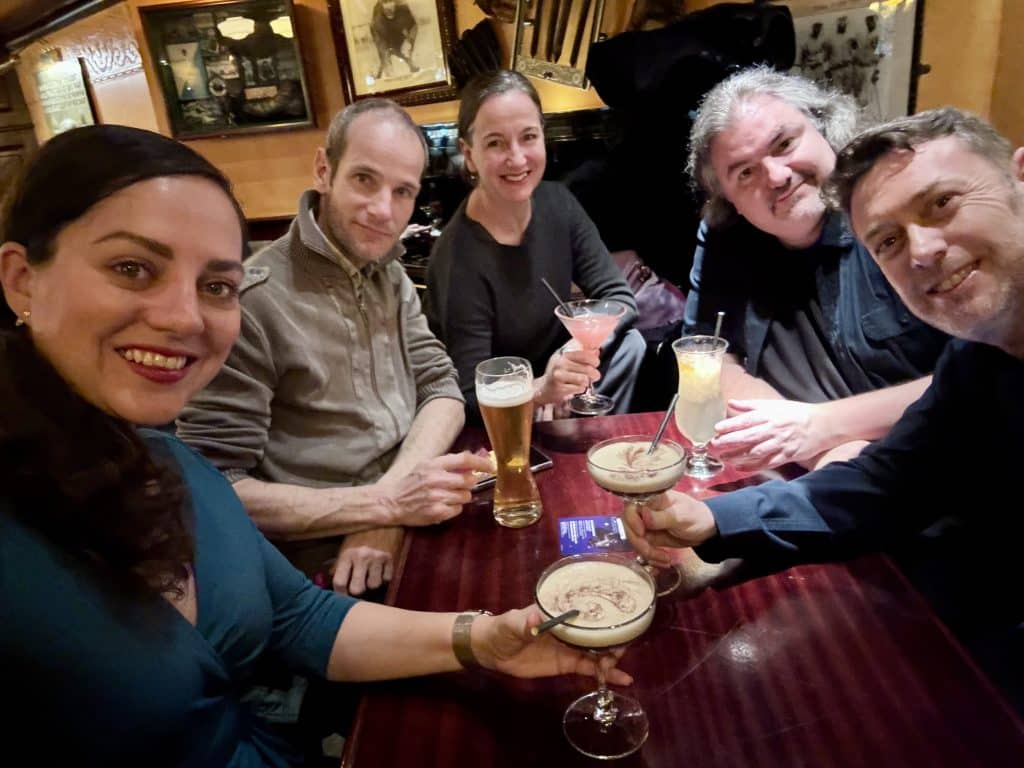 Kate and friends sitting around the table with cocktails and beers in a dark pub.