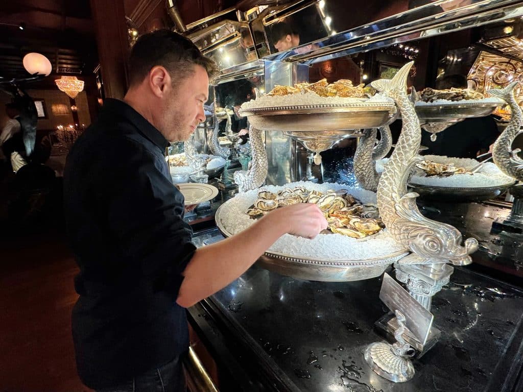 Charlie serves himself oysters from a tray decorated with curving, silver fish.